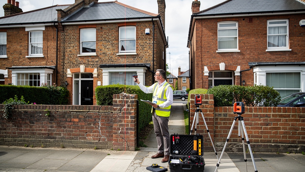 Party wall surveyor measuring and documenting shared boundary wall between two terraced houses in Hounslow